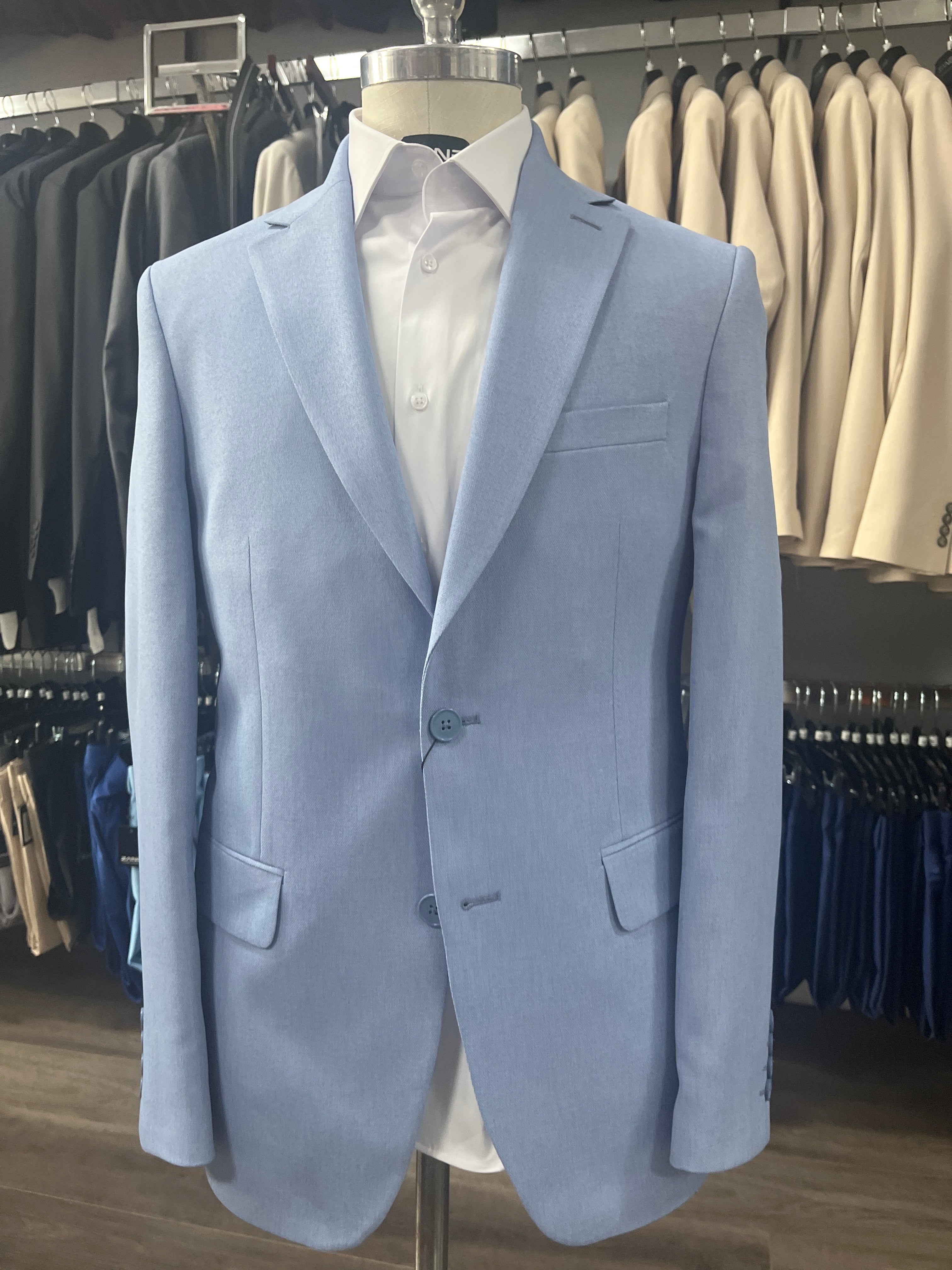 Folded light blue suit jacket on a rack with other clothing items.