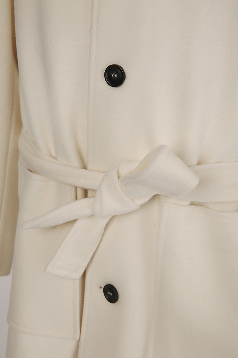 Close-up of a cream-colored coat with a belt and black buttons on a white background